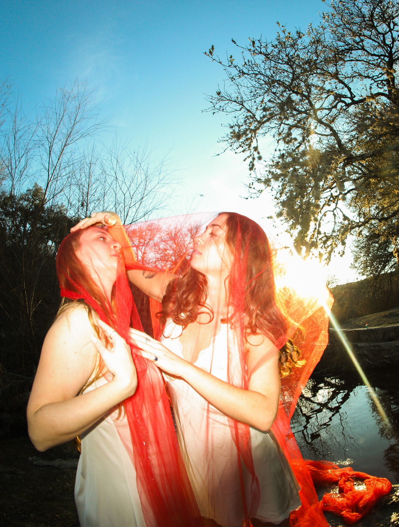 Two dancers wrapped in a red veil against the sun by the water