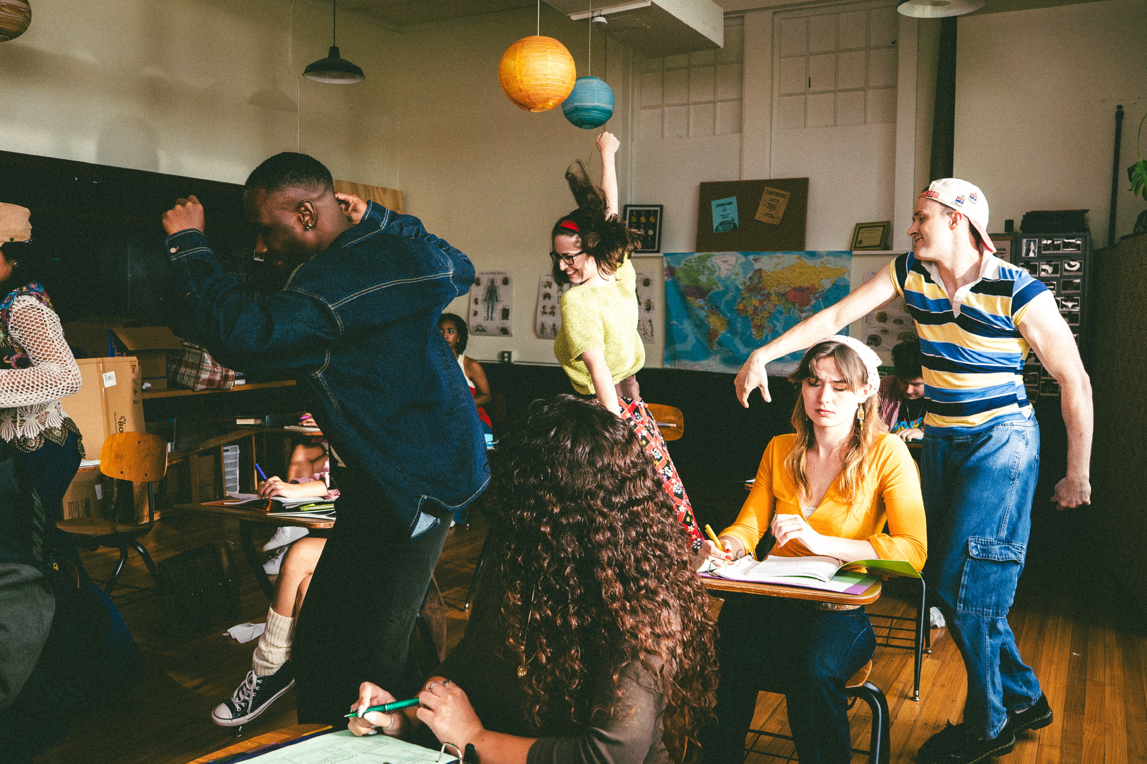 Dancers breaking into choreography between the desks of a 90s classroom